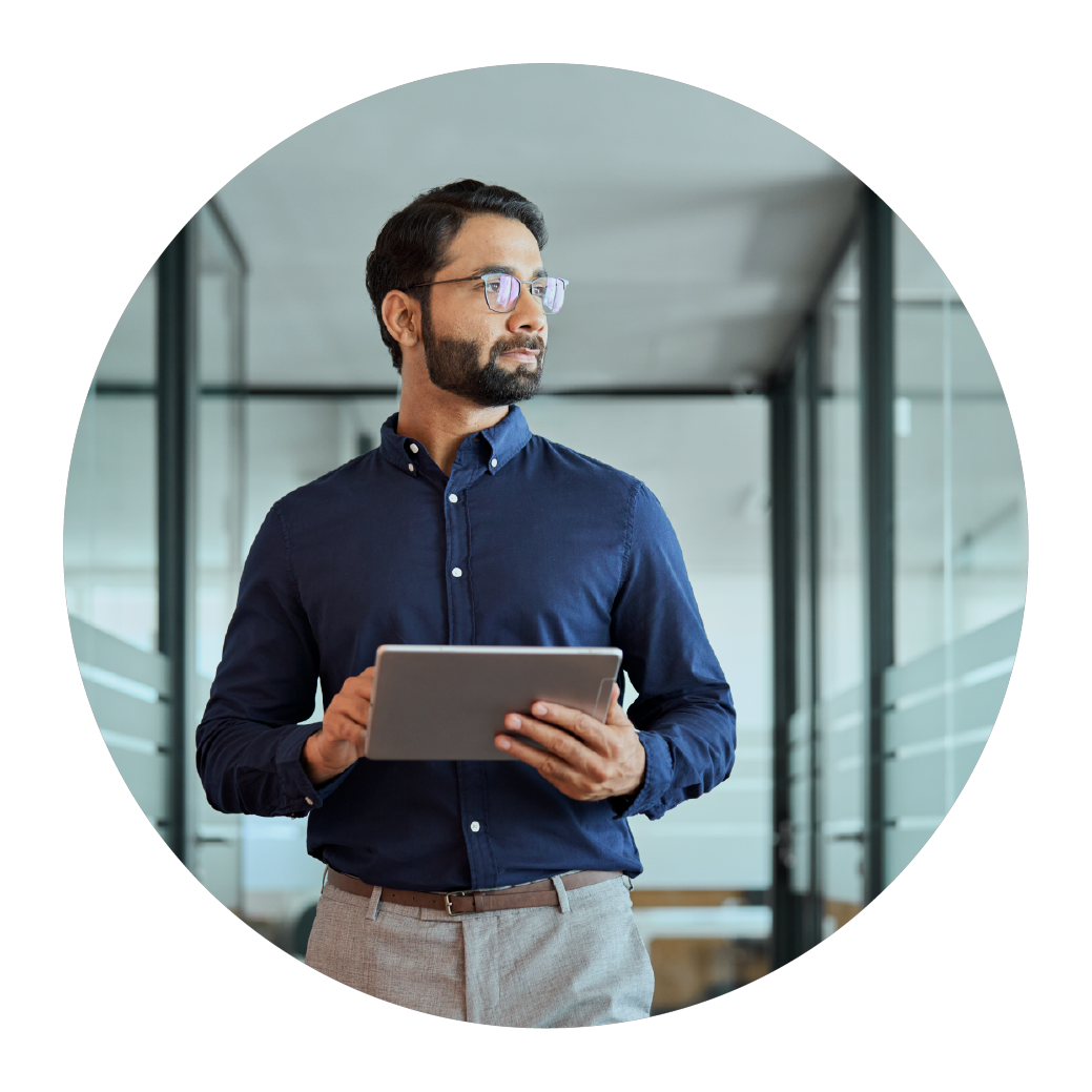 a professional man confidently walking in a sleek office environment while using a tablet, suggesting a scenario where technology meets mobility. He is dressed in a smart blue shirt and gray trousers, indicative of a business casual look. The setting features glass walls and modern architecture, emphasizing a contemporary corporate culture. This image effectively captures the essence of modern business practices, where digital tools enhance productivity and connectivity on the go.