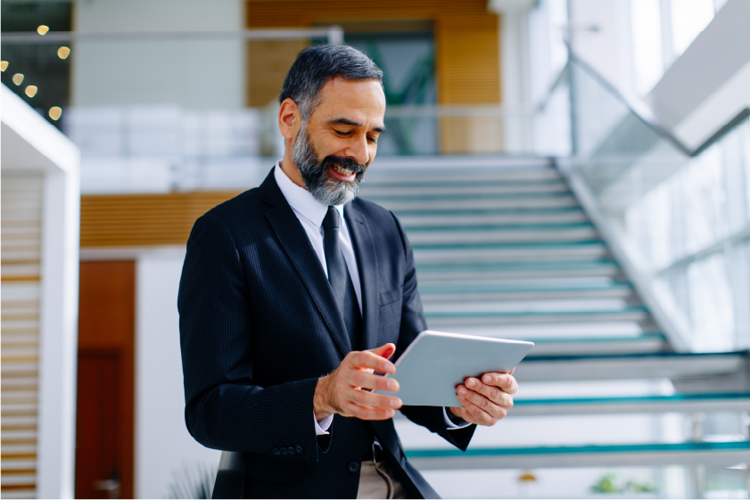 A businessman is standing on a professional buildings open stairwell, smiling at an iPad.