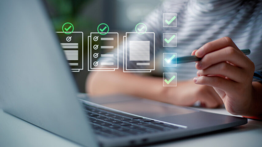 A person uses a stylus to interact with a laptop displaying digital checklists and check marks, representing task completion and document verification. Floating icons with green check marks emphasize compliance and thorough review, with a soft, focused background that underscores a high-tech, digital workspace environment.